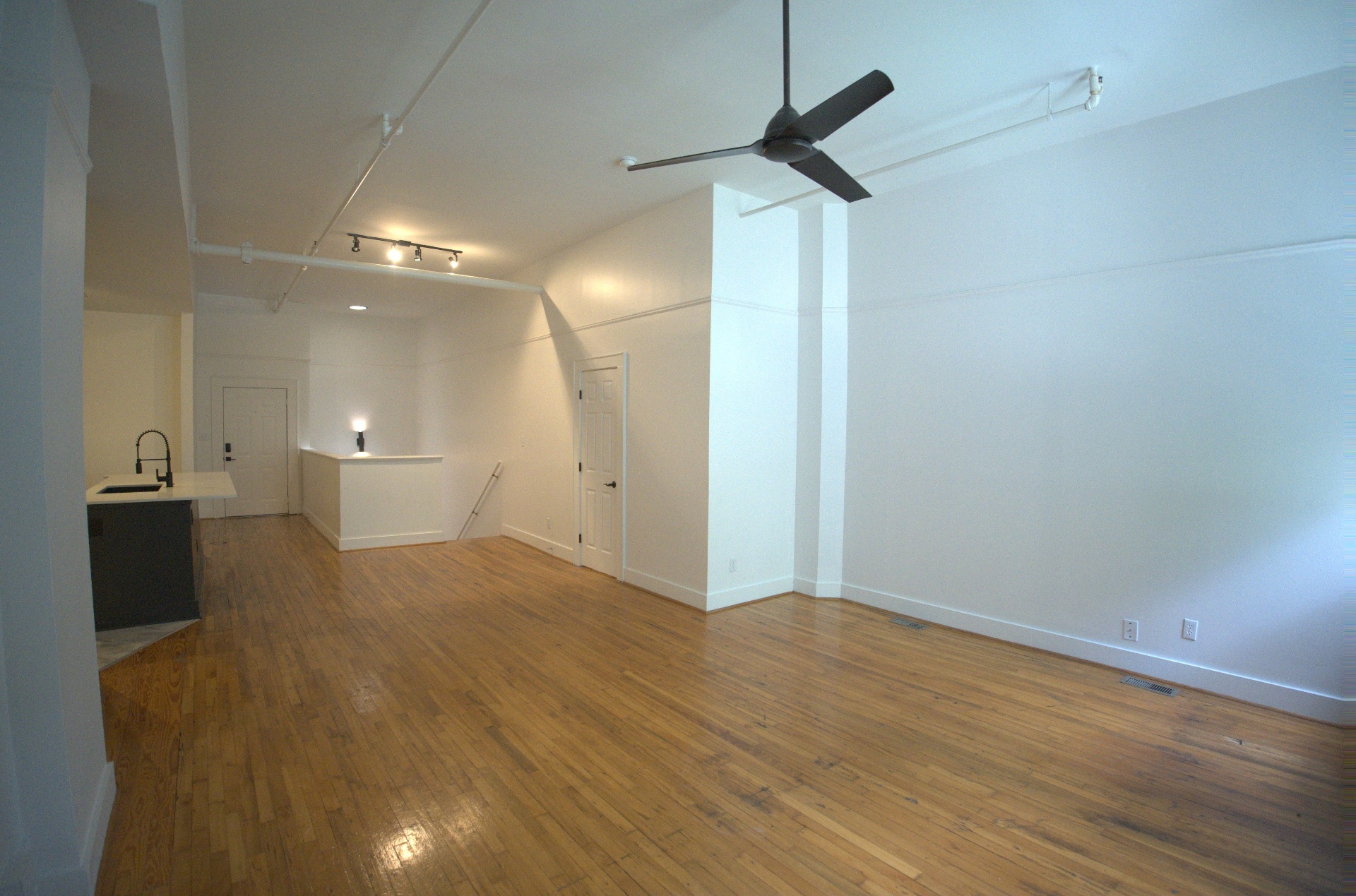 Open loft room with original hardwood floors, white walls and daylight from tall windows